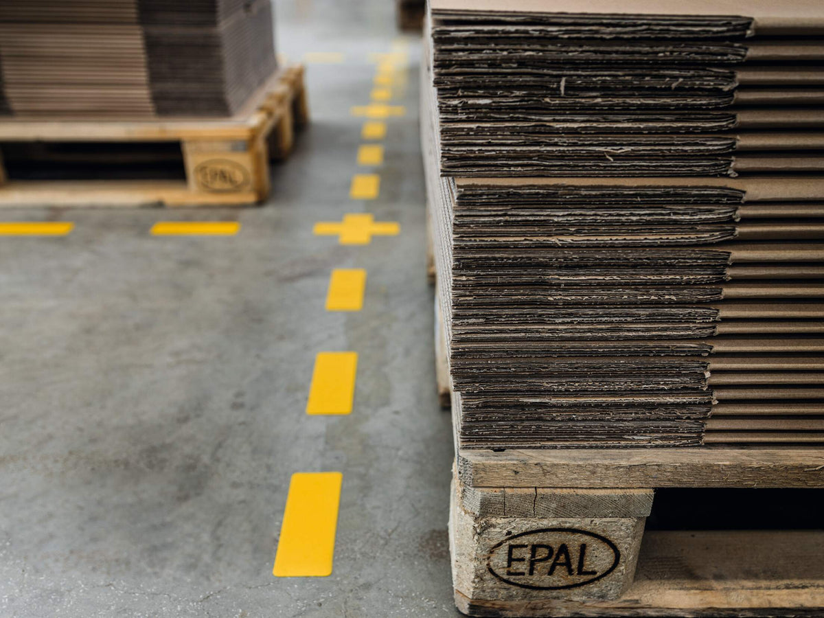 Durable yellow cross joining a dashed line of yellow stripes beside stacked pallets