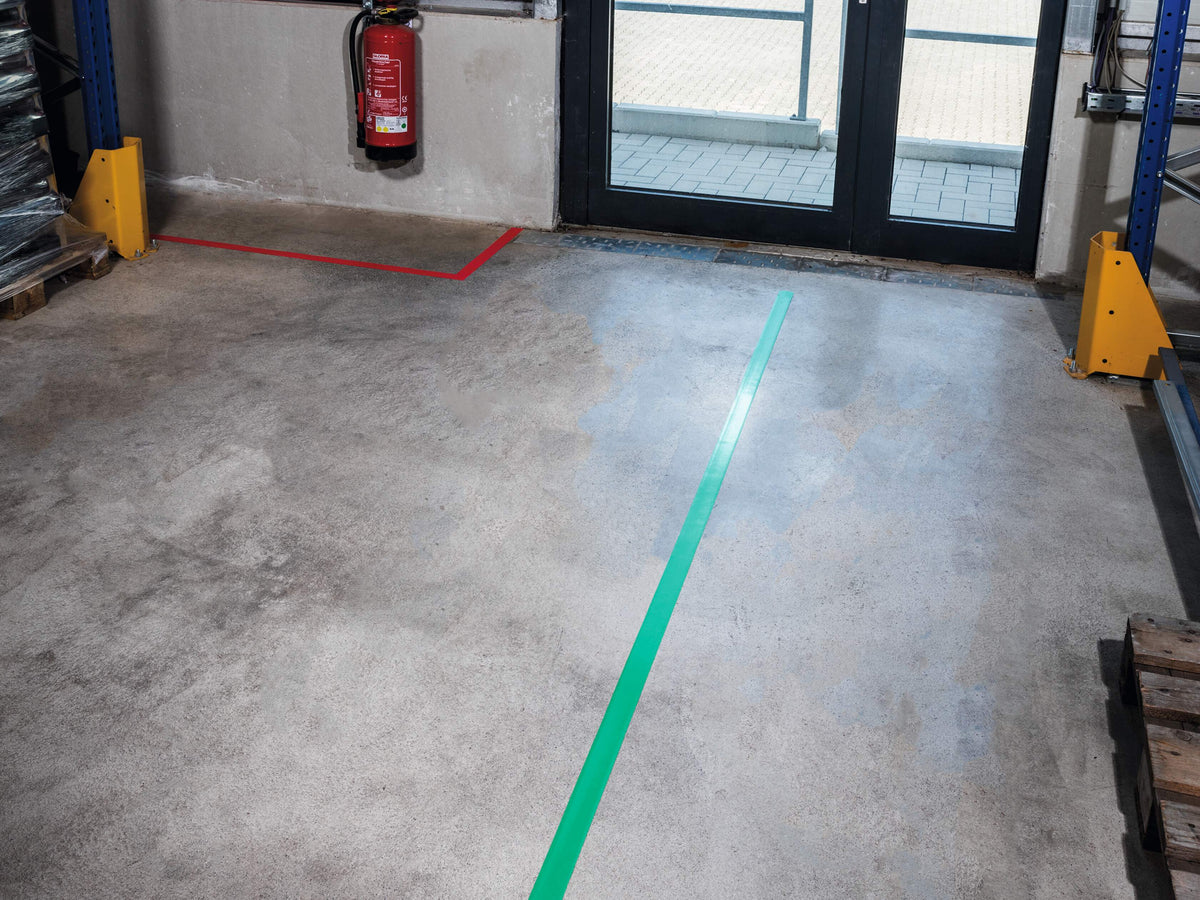 Red DURALINE STRONG line outlining a corner area by a glazed door, with a green line across the warehouse floor