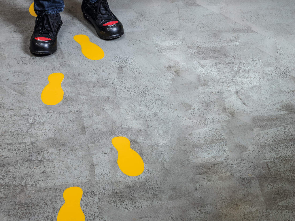 Yellow Durable footprints leading across a concrete floor from a pair of work boots