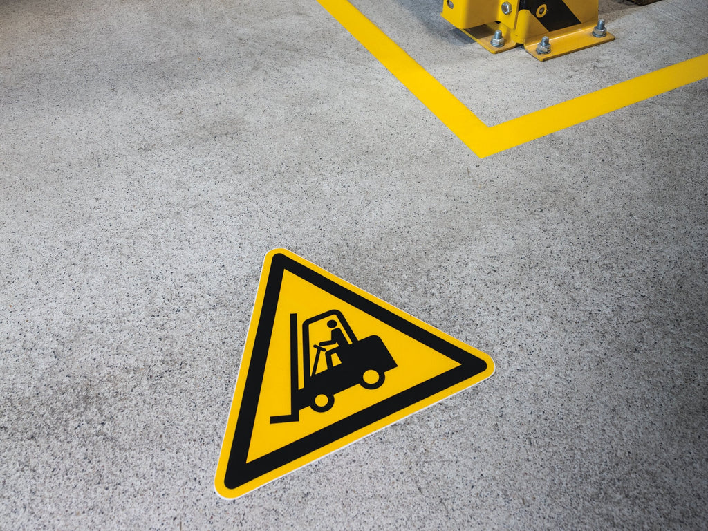 Durable forklift warning triangle laid on a grey floor beside a yellow line